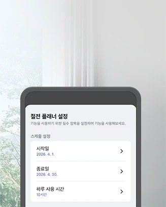 절전 플래너 설정 화면이 스마트폰에 표시되어 있습니다. 화면 상단에는 절전 플래너 설정이라는 제목이 있으며, 그 아래에 기능을 사용하기 위한 필수 항목을 설정하여 기능을 사용해보세요.라는 안내 문구가 있습니다. 스케줄 설정 항목으로는 시작일 2026. 4. 1., 종료일 2026. 4. 30., 하루 사용 시간 10시간이 나열되어 있습니다. 스마트폰 화면은 창문을 배경으로 하여 배치되어 있으며, 창문 밖으로는 나무가 보입니다. 제품의 색상은 흰색이며, 벽에 설치된 모습입니다.